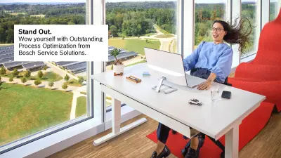 A lady is sitting at a desk, staring excitedly at the screen in front of her with wide eyes. She looks as if she has been blown backwards, her hair is flying and she is holding on to the desk.