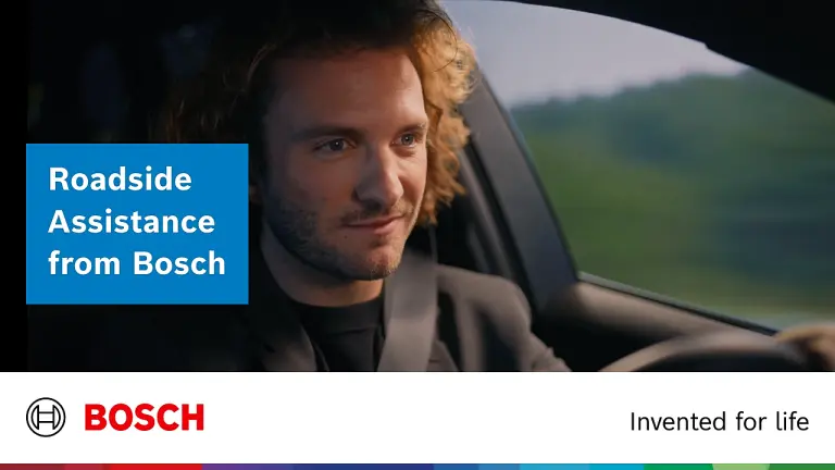 A curly-haired man sits in his car behind the steering wheel and smiles.