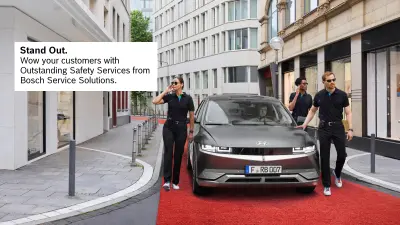 A driver drives his vehicle through a street in a city center, accompanied by three people who look like security guards. The vehicle drives on a red carpet.