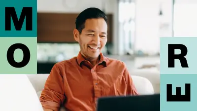 Ein Mann in einem orangenen Shirt sitzt auf seiner Couch und schaut lächelnd in den Bildschirm seines Laptops der sich vor ihm befindet. 