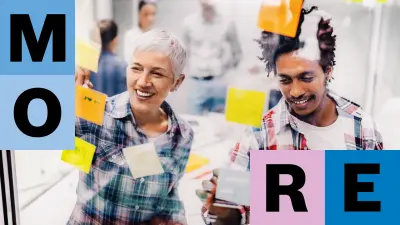 Ein Frau mit grauem, kurzgeschnittenen Haar steht mit einem männlichen Kollegen vor einer transparenter Metaplanwand, sie beschriften bunte Post-its und kleben sie lächelnd an die Wand. Im Hintergrund sind leicht verschwommen weitere Mitarbeitende zu sehen. 