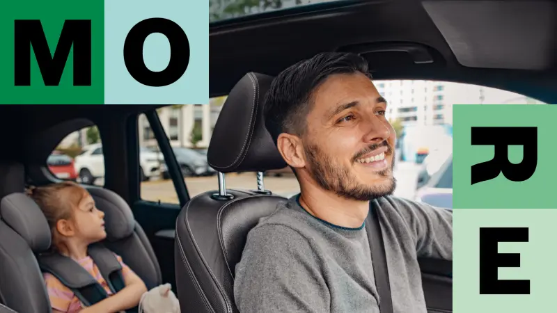 A man is sitting smiling in the driver's seat of his vehicle, with his daughter sitting in a child seat in the back.