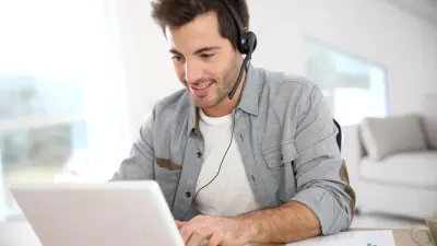 Mann mit Headset schaut lächelnd auf den Bildschirm seines Laptops