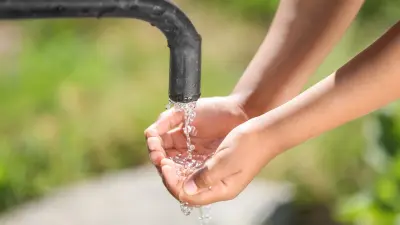 A person catches water from a faucet with their hands clasped.