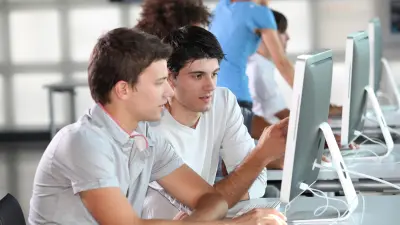 Two students sit in front of a laptop and talk