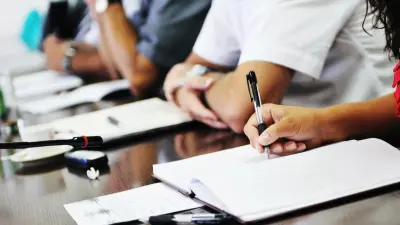 People sit next to each other in a row, one person writes something on a pad