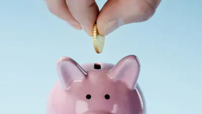 A hand throws a coin into a pink piggy bank