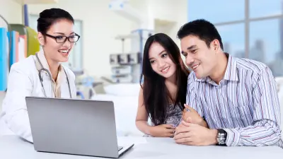 A couple looks at a laptop together with a doctor