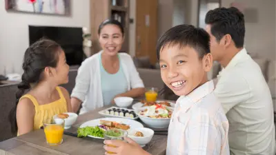 A Vietnamese family is sitting at the kitchen table while eating, mother and son look at the camera smiling.