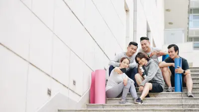 A group of Vietnamese employees are sitting on a staircase with yoga mats and taking a selfie.