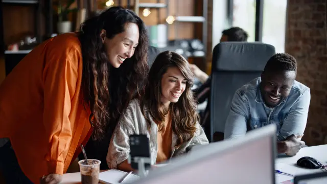 A group of colleagues look together at a screen on a desk.