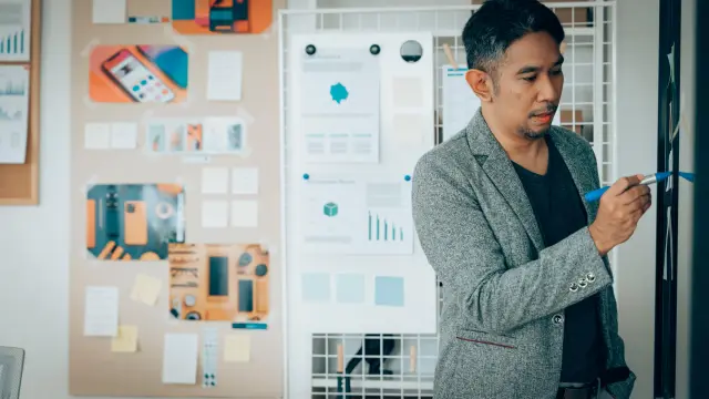 A UX designer stands in front of a metaplan board and draws something on it.