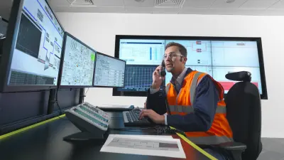 A facility manager sits in his office, talking on the phone and looking at the screens in front of him.