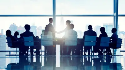 Eine Gruppe von Kollegen und Kolleginnen sitzt um einen Meetingtisch. Im Hintergrund ist die Skyline einer Stadt zu sehen.