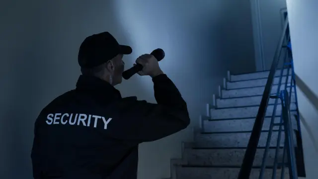 Ein Mitarbeiter einer Sicherheitsfirma leuchtet mir einer Taschenlampe in ein dunkles Treppenhaus.