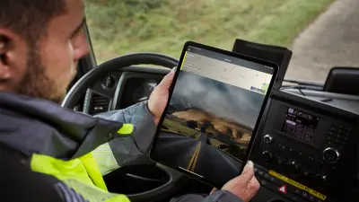 Ein Servicetechniker steht vor einem Fahrzeug und schaut auf ein Tablet.