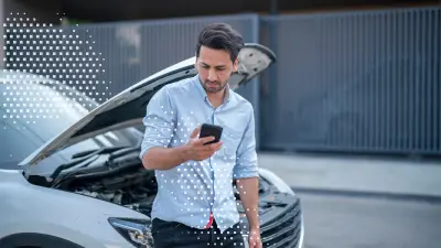 A man is leaning against his vehicle, looking at his smartphone. It is visible that the hood of his car is open.
