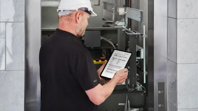 Ein Techniker steht vor einem Aufzug und schaut auf ein Tablet.