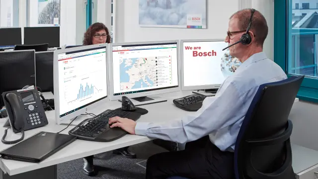 Mitarbeiter mit Headset sitzt im Monitoring Center vor zwei Bildschirmen