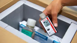 A person holds a so-called data logger from Elpro and places it with refrigerated medicines.