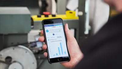 A technician holds a smartphone in his hand and looks at the display. Data from elevator monitoring can be seen on the screen.