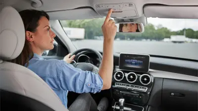 A woman sits in the driver's seat in the car and presses the eCall button.
