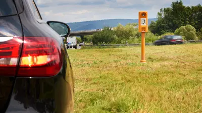 Ein schwarzes Auto steht am Rande der Autobahn, im Hintergrund ist eine Notrufsäule zu sehen. 