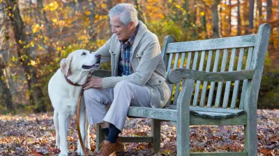 Ein älterer Herr sitzt auf einer Parkbank und streichelt seinen Hund. 