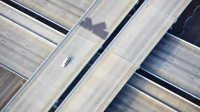 Ein Auto fährt auf einer leeren Autobahn, dahinter sieht man den Schatten eines Satelliten. 