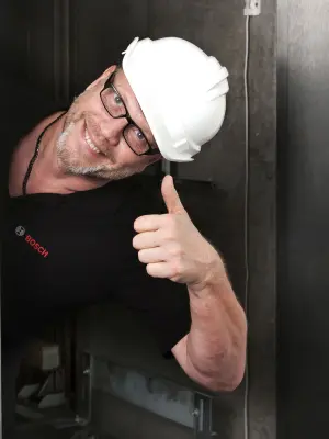 Detlef looks out from an elevator shaft and gives a thumbs up. He is wearing a safety helmet.
