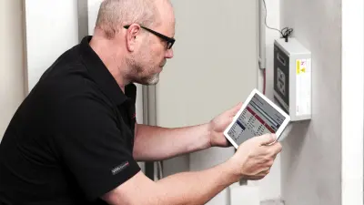  Detlef crouches over a measuring instrument. He looks at a tablet. 