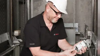 Detlef sits in the elevator shaft and looks at a measuring instrument. He is wearing a safety helmet.