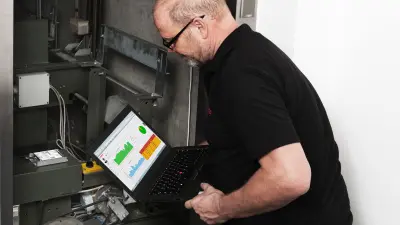 Detlef crouches over an elevator shaft. He looks at the laptop perched on his lap.