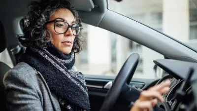 Fahrerin eines Fahrzeugs sitzt vor dem Lenkrad und bedient ein Smartphone