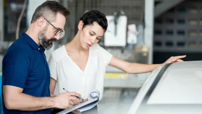 Der Flottenmanager und die Fahrerin stehen neben dem Auto und schauen gemeinsam auf ein Übergabeprotokoll