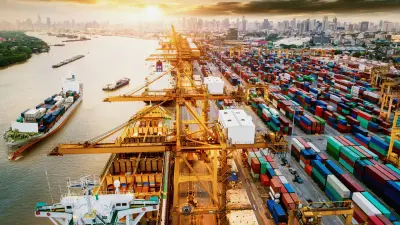 On the left side of the picture, ships are sailing on a river, while on the right side a cargo port with cranes, containers and cars can be seen.