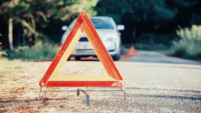 A car stands at the side of a road. In the front of the image is a safety triangle on the ground.