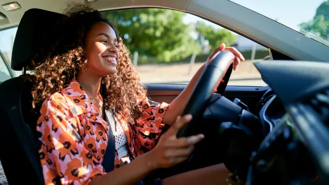 A woman with long brown curls sits smiling behind the wheel of her vehicle.