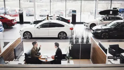 View from above into the showroom of a car dealership; you can see two people sitting in a lounge; various vehicles can be seen in the background