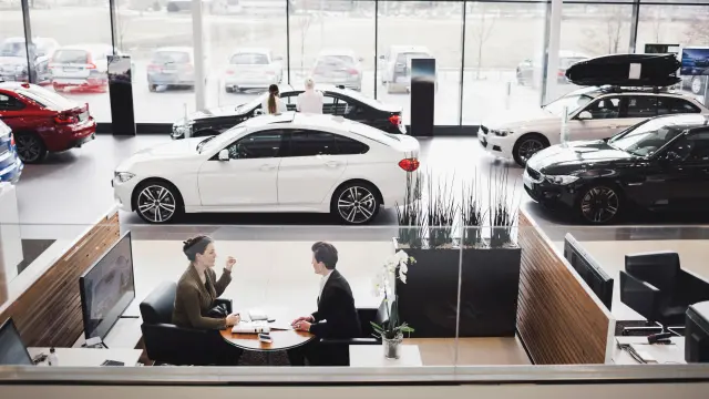 View from above into the showroom of a car dealership; you can see two people sitting in a lounge; various vehicles can be seen in the background