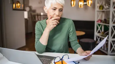An elderly lady with gray hair looks at various documents that she is holding in her hands. 