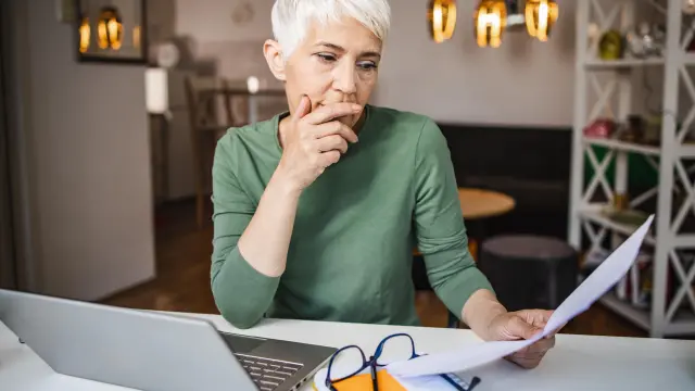 An elderly lady with gray hair looks at various documents that she is holding in her hands. 