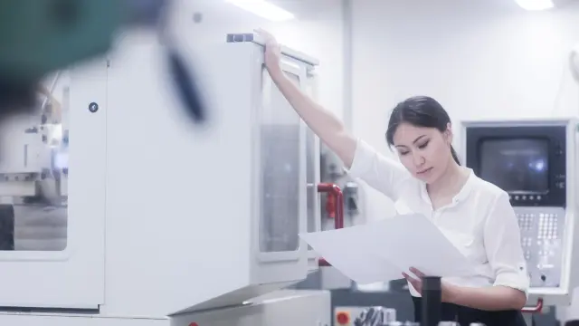 An employee in a laboratory stands in front of a medical device and looks questioningly at an instruction manual.